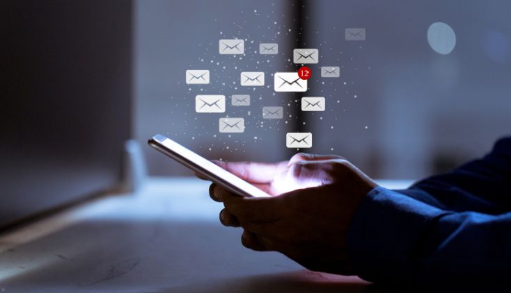 A person holding a cell phone, with envelope icons around it to indicate emails.
