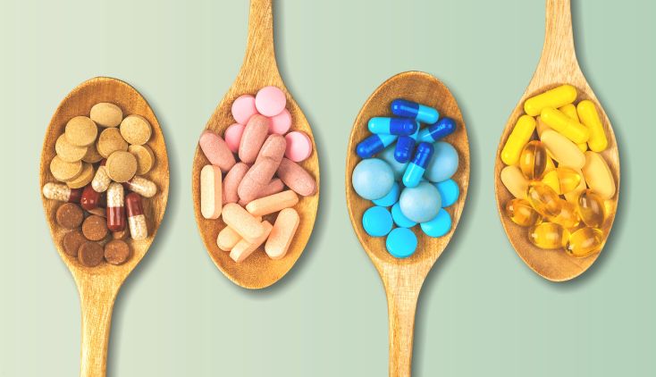 Four wooden spoons holding supplement pills of different colors.