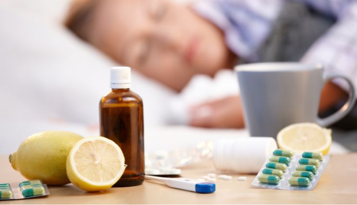 Different natural and medical cold and flu treatments on a bedside table. A person is sleeping in the background.