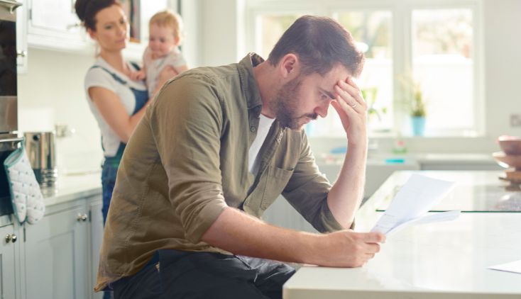 A man sitting at a table, looking at paperwork. He has a frustrated expression.