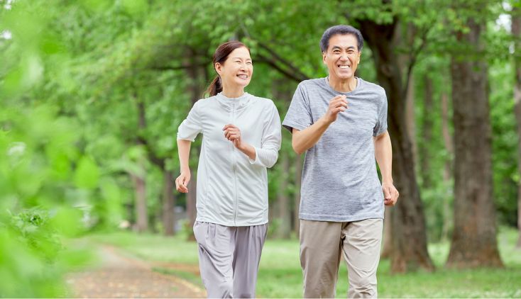 An older couple in grey outfits running on a trail.