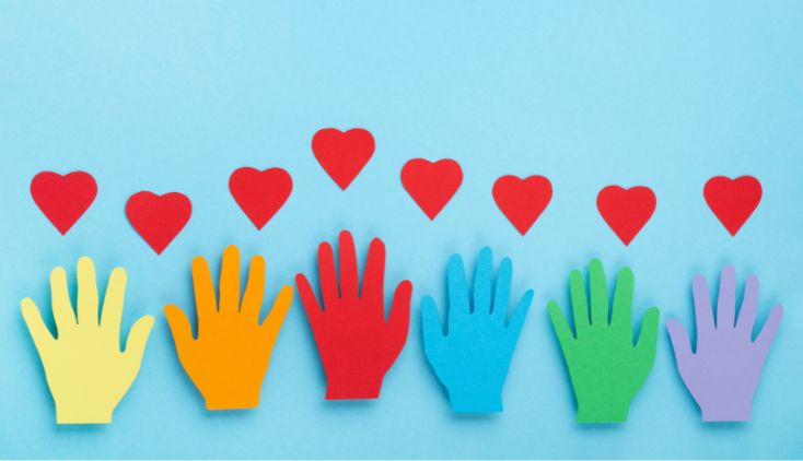 Multi-colored paper cutouts of hands on a blue background, with red hearts above them.