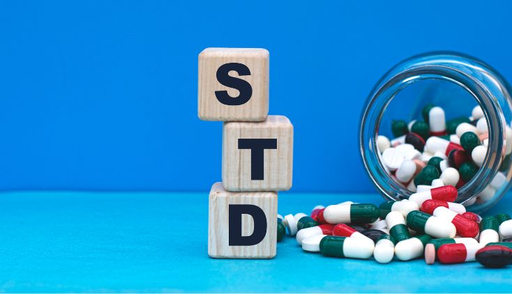 A bottle of pills spilling out with square blocks that spell STD against a blue background.