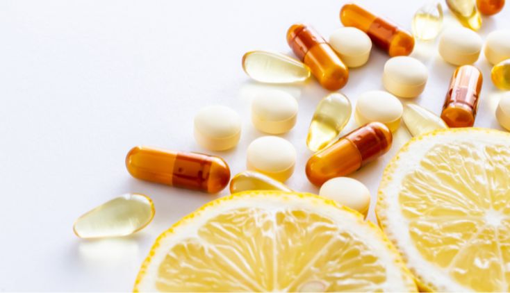 White and orange supplement pills on a white surface with slices of lemon.