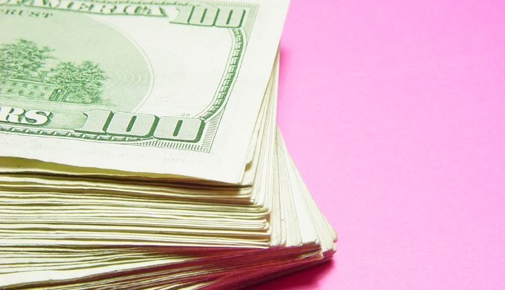 A pile of $100 bills on a pink background.
