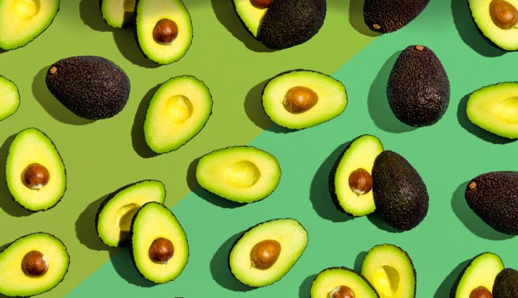 Avocados cut in half on a green background.
