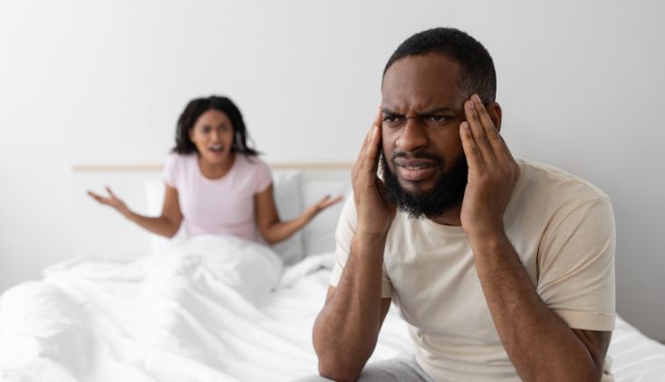 A man and woman sitting in a bed, looking stressed and confused.
