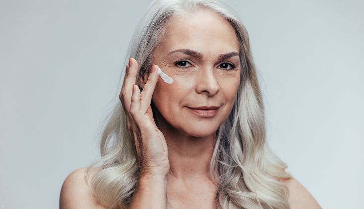 An older woman putting moisturizer on her face.