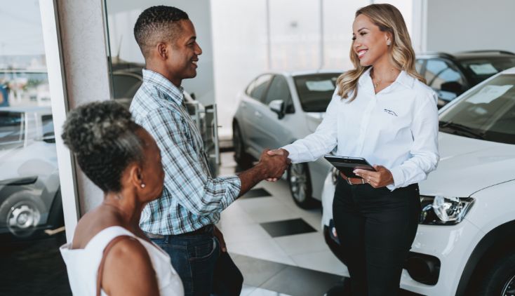 A couple standing in a car dealership, talking to a saleswoman