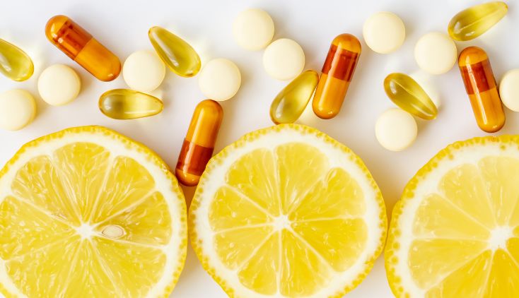 Different types of vitamin pills on a white table with slices of lemon.